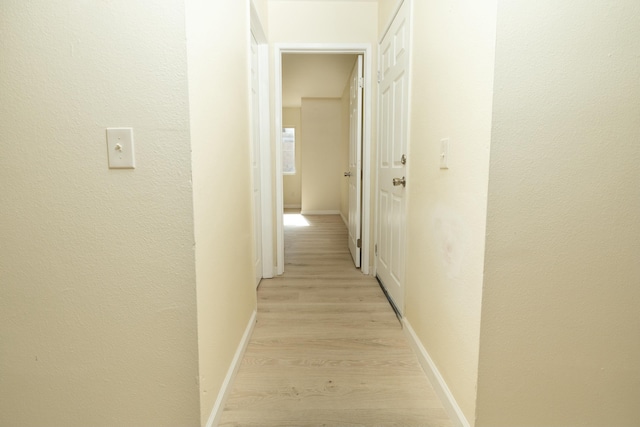 hall with light wood-type flooring, baseboards, and a textured wall