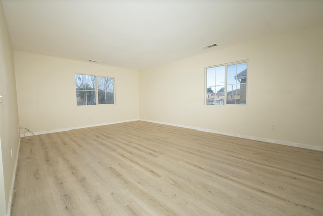 empty room featuring light wood-type flooring, visible vents, and baseboards