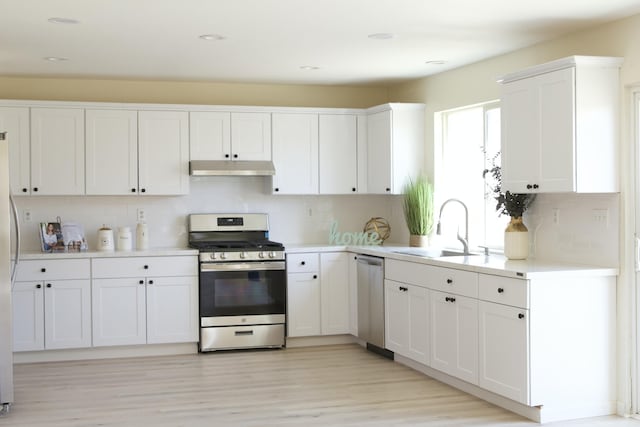 kitchen featuring light countertops, appliances with stainless steel finishes, white cabinets, a sink, and under cabinet range hood