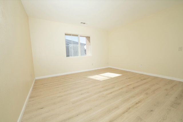 empty room with light wood finished floors, visible vents, and baseboards