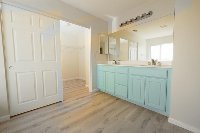 full bath featuring a sink, a spacious closet, double vanity, and wood finished floors