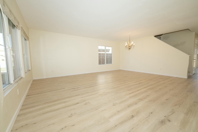 spare room with an inviting chandelier, baseboards, and light wood finished floors