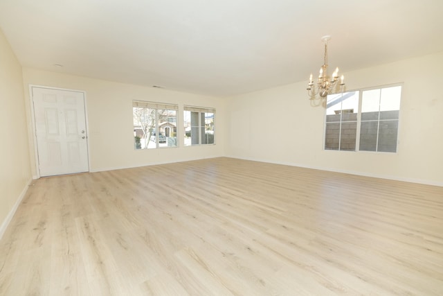 spare room featuring light wood-style floors, baseboards, and an inviting chandelier