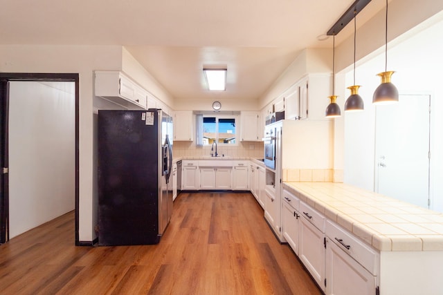 kitchen featuring white cabinets, appliances with stainless steel finishes, tile counters, and pendant lighting