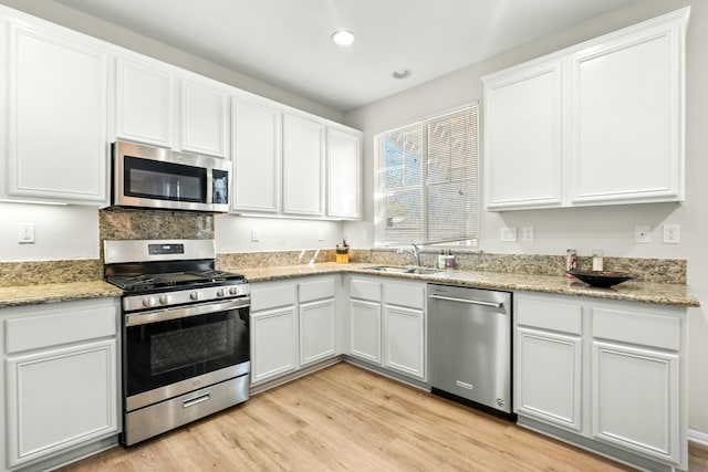 kitchen featuring light stone counters, stainless steel appliances, sink, light hardwood / wood-style floors, and white cabinetry