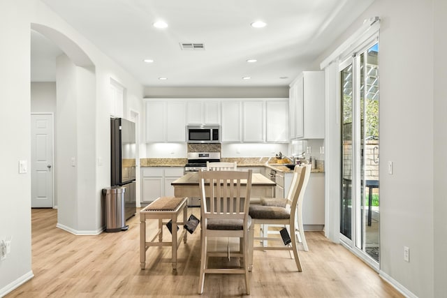 kitchen featuring stainless steel appliances, light stone counters, light hardwood / wood-style flooring, a breakfast bar area, and white cabinets