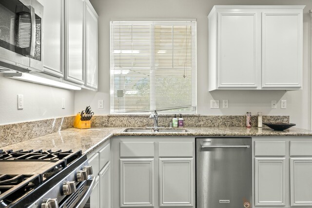 kitchen with light stone countertops, white cabinetry, sink, and appliances with stainless steel finishes