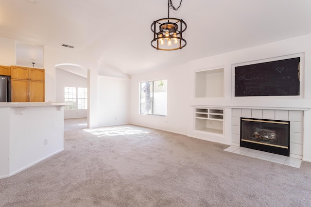 unfurnished living room featuring a tiled fireplace, vaulted ceiling, light carpet, and a chandelier