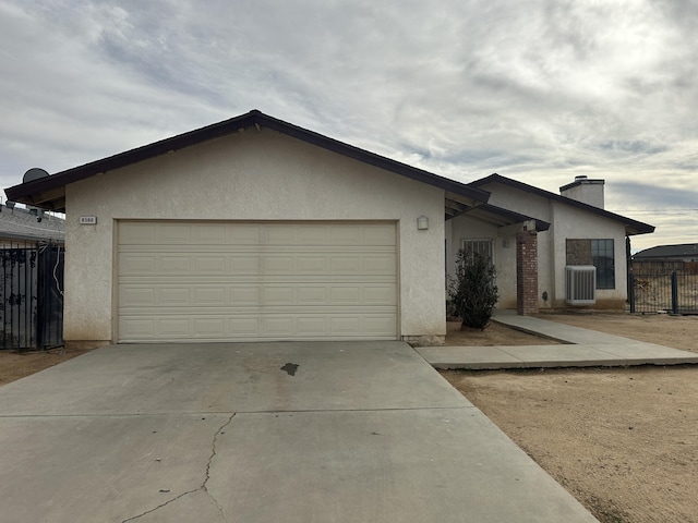 view of front facade with stucco siding, an attached garage, central AC, fence, and driveway