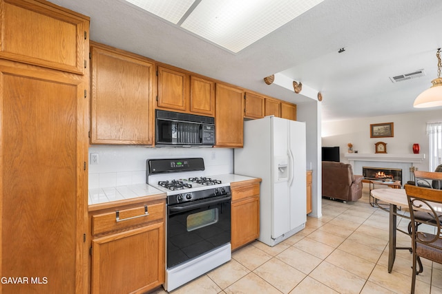 3167 Hampton Rd, Palmdale, CA 93551 - kitchen with black appliances, tile counters, open floor plan, light tile patterned flooring, and a glass covered fireplace