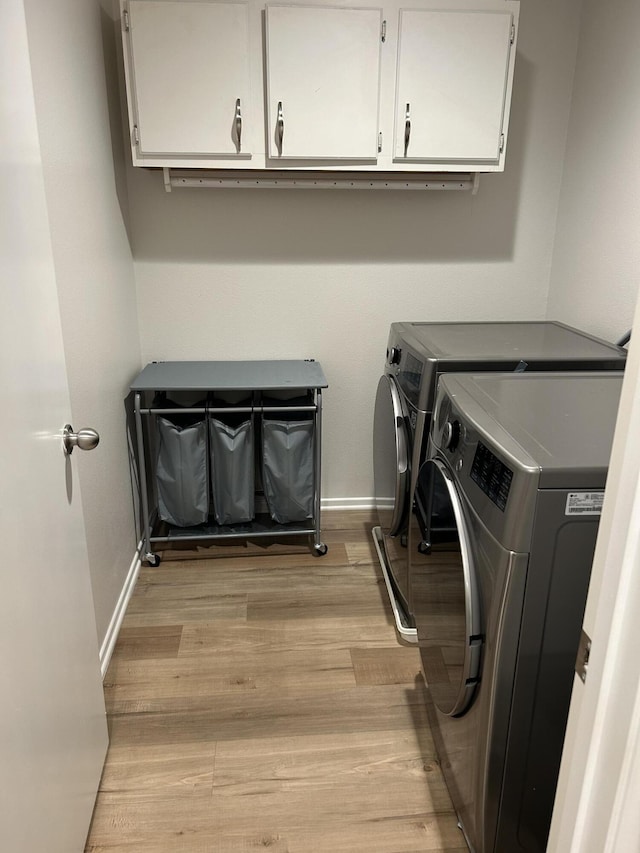 laundry room featuring washer and dryer, light wood-type flooring, and cabinets