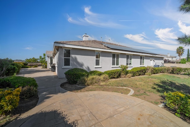 rear view of house with roof mounted solar panels, stucco siding, a chimney, and a lawn