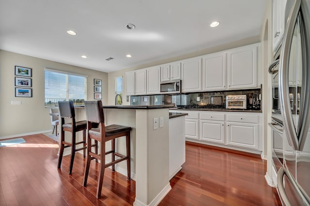 kitchen featuring stainless steel microwave, a breakfast bar, refrigerator, dark wood-style floors, and dark countertops