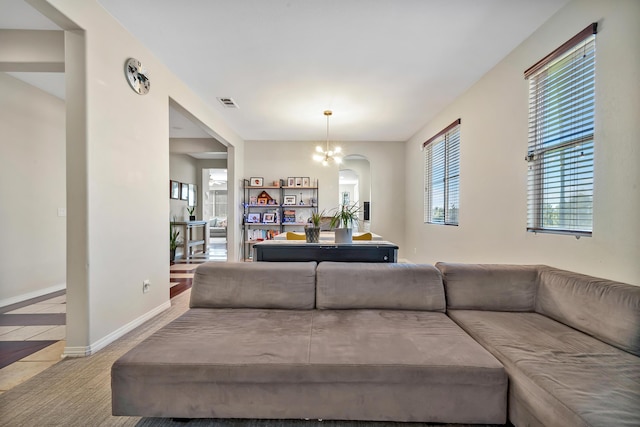 carpeted living area featuring visible vents, baseboards, arched walkways, and a notable chandelier