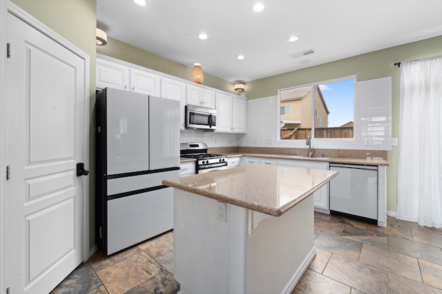 kitchen with stone tile floors, a kitchen island, a sink, stainless steel appliances, and white cabinetry