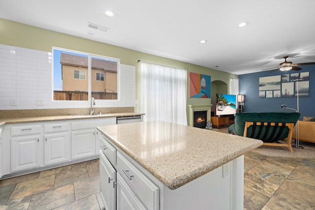 kitchen with a center island, dishwasher, a lit fireplace, white cabinetry, and a sink