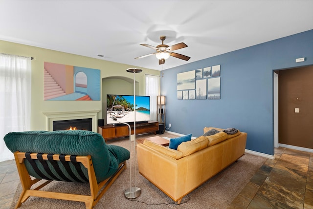 living room with visible vents, ceiling fan, a warm lit fireplace, and baseboards