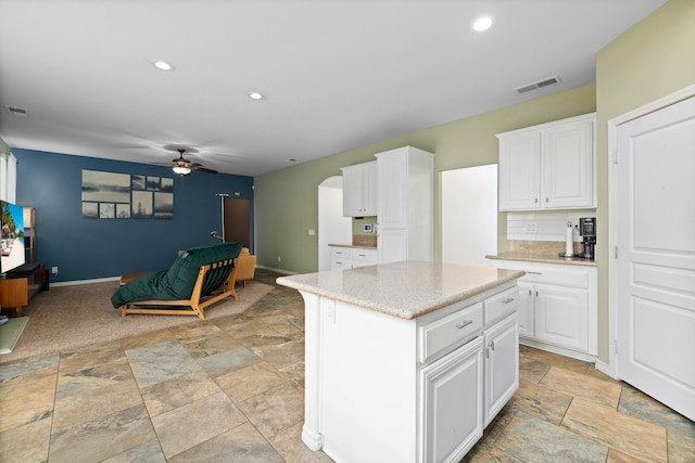 kitchen featuring visible vents, open floor plan, arched walkways, white cabinets, and a ceiling fan