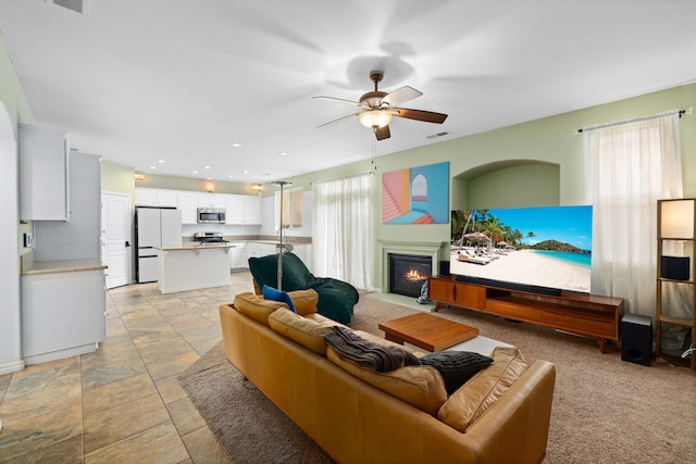 living room with ceiling fan, visible vents, a healthy amount of sunlight, and a glass covered fireplace