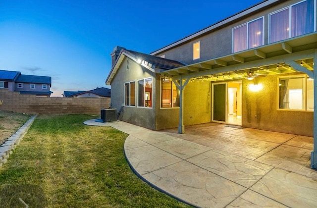 back of property with central AC unit, fence, a lawn, stucco siding, and a patio area