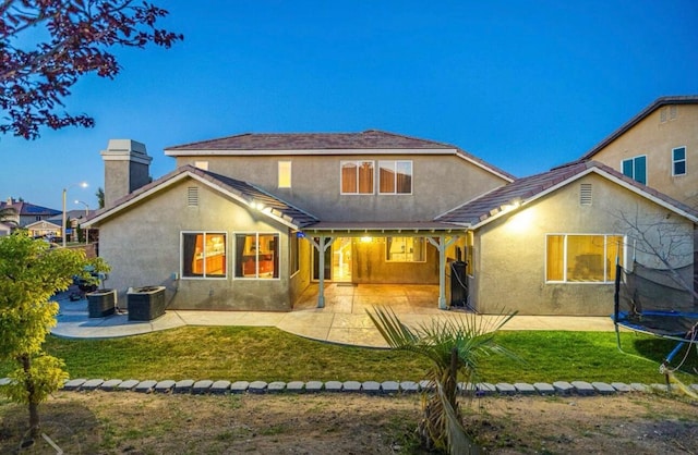 rear view of house featuring a trampoline, a yard, stucco siding, a patio area, and cooling unit