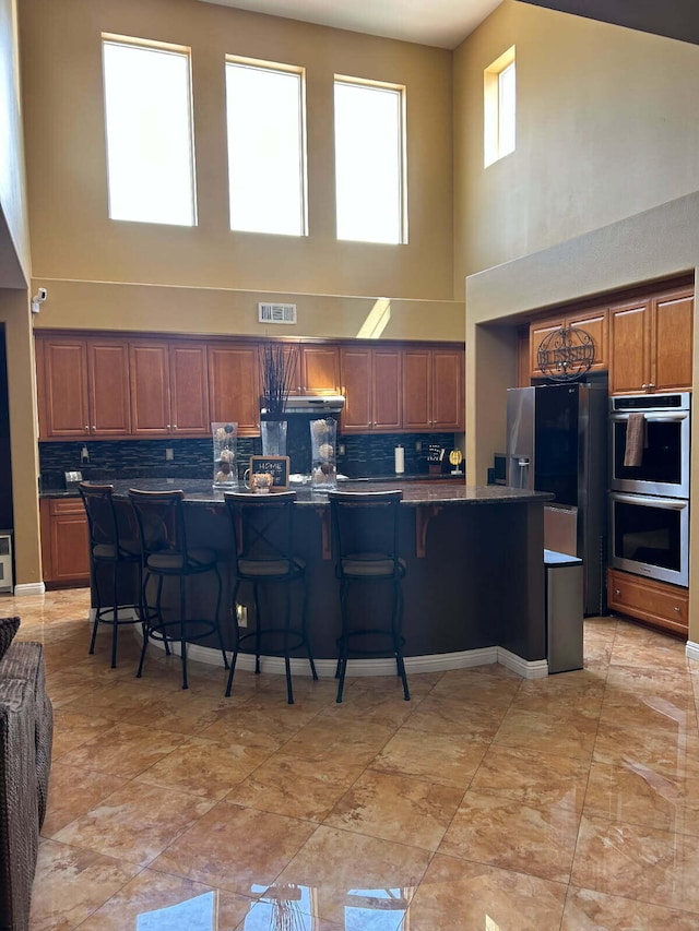 kitchen with backsplash, a high ceiling, appliances with stainless steel finishes, and visible vents