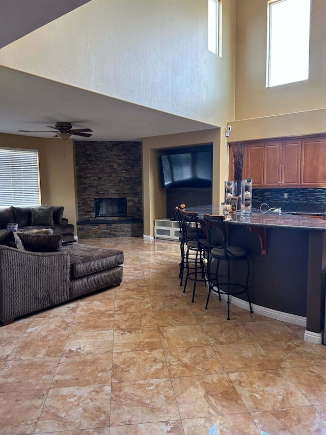 interior space featuring a stone fireplace, a high ceiling, and a ceiling fan