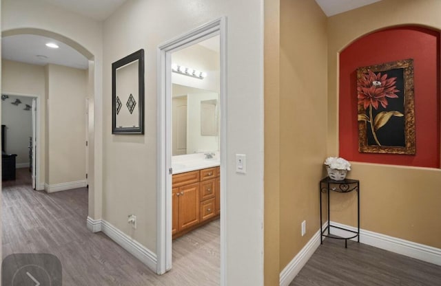 hallway with light wood finished floors, baseboards, and arched walkways