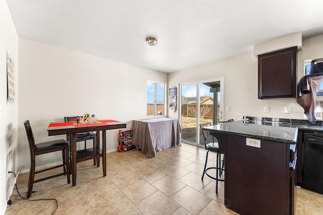 kitchen featuring dark brown cabinets, baseboards, a breakfast bar, black dishwasher, and dark stone countertops