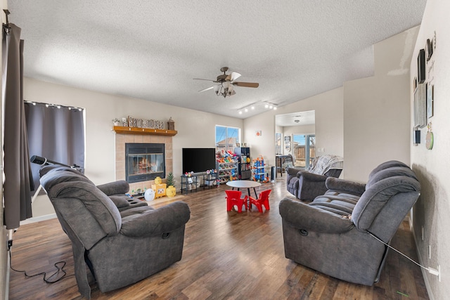 living room with ceiling fan, vaulted ceiling, a tile fireplace, wood finished floors, and a textured ceiling