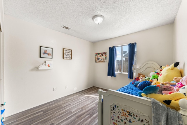 bedroom featuring visible vents, baseboards, a textured ceiling, and wood finished floors