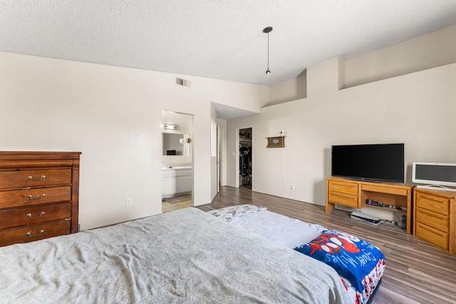 bedroom with visible vents, a textured ceiling, wood finished floors, connected bathroom, and vaulted ceiling