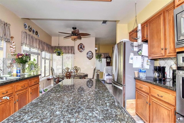 kitchen featuring ceiling fan, sink, stainless steel appliances, tasteful backsplash, and dark stone countertops