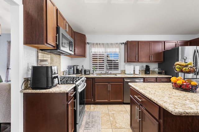 kitchen with light stone countertops, sink, appliances with stainless steel finishes, and light tile patterned flooring