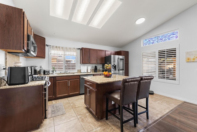 kitchen with appliances with stainless steel finishes, vaulted ceiling, a kitchen island, a breakfast bar, and sink