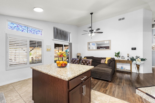 kitchen with dark brown cabinetry, a center island, lofted ceiling, light tile patterned flooring, and ceiling fan