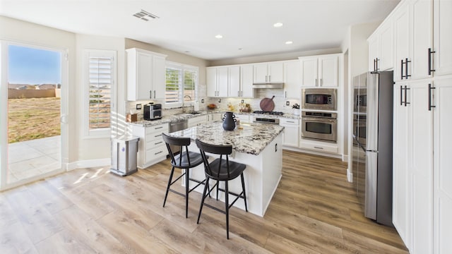 3929 Derby Cir, Quartz Hill, CA 93536 - kitchen featuring appliances with stainless steel finishes, a center island, under cabinet range hood, a breakfast bar area, and white cabinets