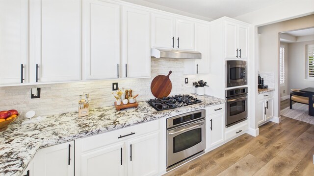 3929 Derby Cir, Quartz Hill, CA 93536 - kitchen with appliances with stainless steel finishes, under cabinet range hood, white cabinets, tasteful backsplash, and light wood finished floors