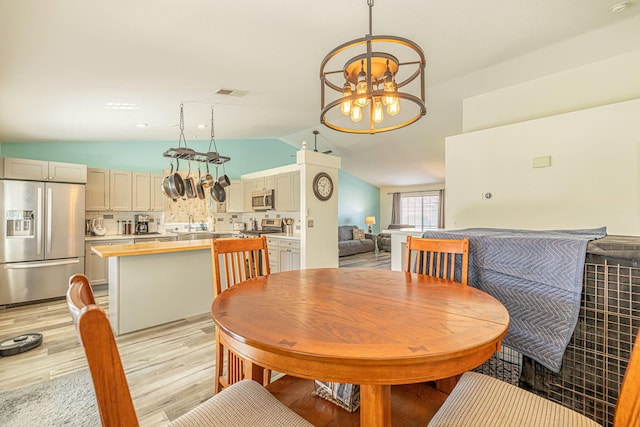 dining area with light wood finished floors, a chandelier, visible vents, and vaulted ceiling