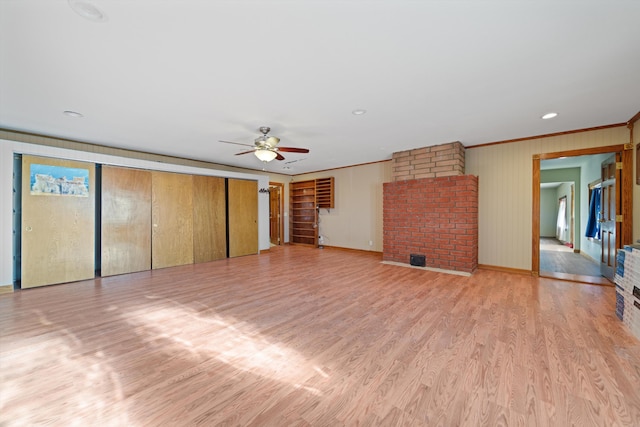 unfurnished living room featuring ceiling fan, wood walls, light wood-type flooring, and crown molding