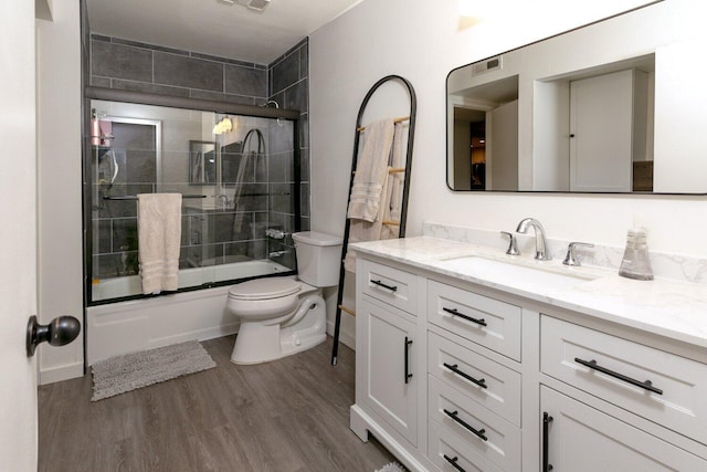 full bathroom featuring vanity, wood finished floors, visible vents, bath / shower combo with glass door, and toilet