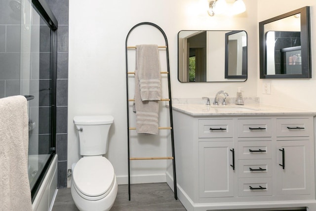 bathroom with baseboards, toilet, wood finished floors, shower / bath combination with glass door, and vanity