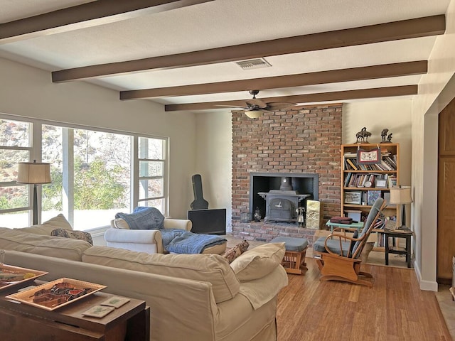 living room featuring a wood stove, ceiling fan, hardwood / wood-style floors, and beamed ceiling