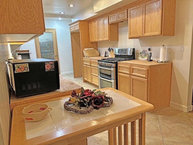 kitchen featuring tile countertops, light brown cabinetry, light tile patterned flooring, and range with two ovens