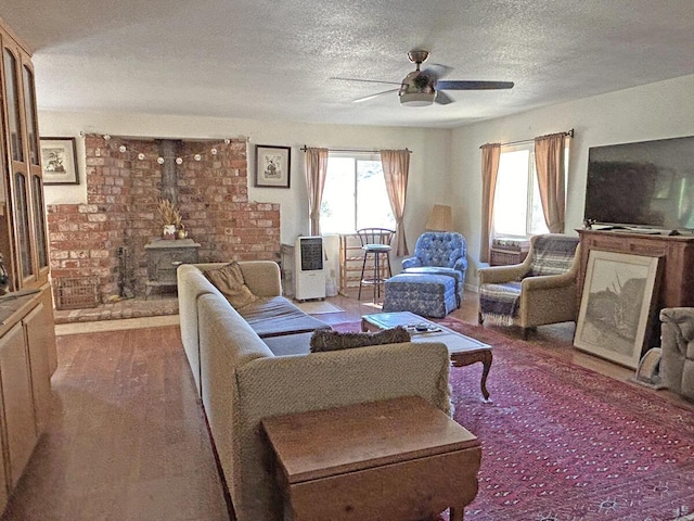 living room with ceiling fan, wood-type flooring, a wood stove, and a textured ceiling