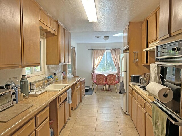 kitchen with sink, oven, white fridge, a textured ceiling, and light tile patterned flooring