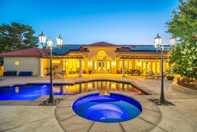 pool at dusk featuring a patio area, an in ground hot tub, and french doors