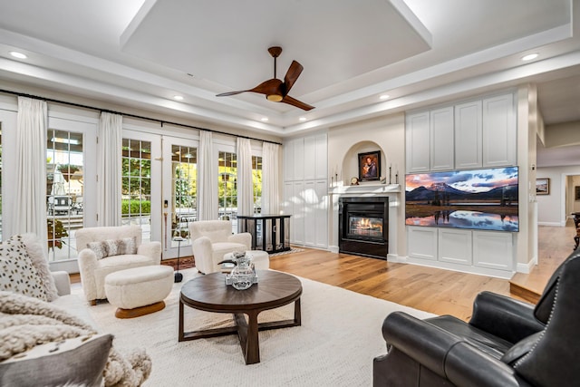 living room with light wood-type flooring, a tray ceiling, and ceiling fan