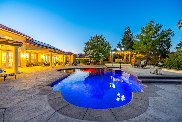 pool at dusk featuring an in ground hot tub, a patio, and pool water feature