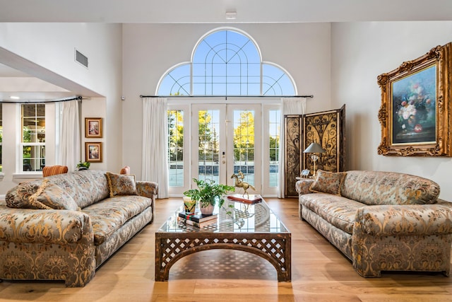 living room with french doors, a towering ceiling, and light hardwood / wood-style flooring